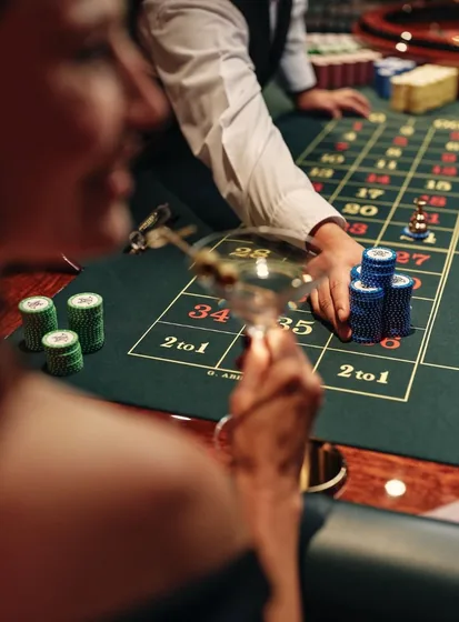 A guest with a cocktail at the roulette table as the dealer sets chips on the layout
